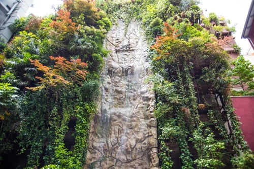 Une cascade artificielle s'écoule le long d'une paroi rocheuse texturée, entourée d'une végétation luxuriante qui recouvre