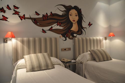 A bedroom with two single beds, headboards with vertical stripes, and a mural of a woman with long hair and red butterflies.