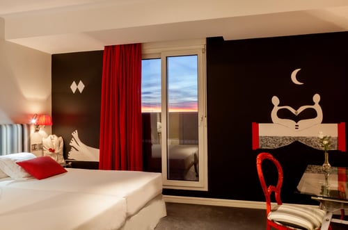 A room with modern decor in shades of black, red, and white, featuring a wall with an abstract mural, a bed with a red