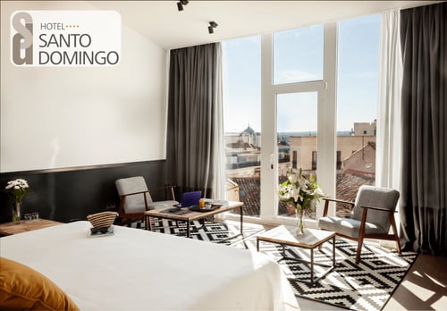 A corner room at the Hotel Santo Domingo with large windows, modern furniture, two armchairs, a coffee table, and views of