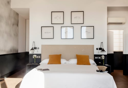 Double bedroom with a large bed, a light-colored fabric headboard, and mustard-colored pillows. White walls with fish-themed