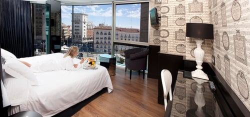 Superior double room with panoramic views of the city, decorated with musical wallpaper, modern furniture, and a white bed.
