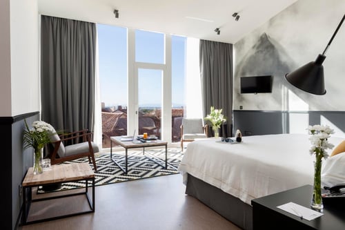 A modern room with a large window offering views of the city rooftops, decorated in neutral tones with wooden furniture and