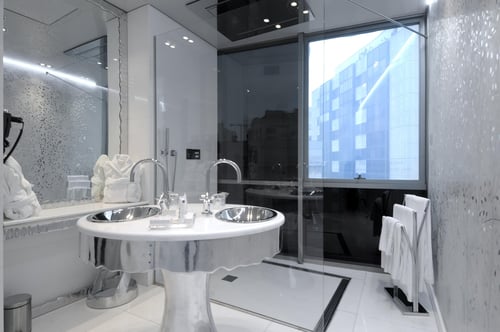 A modern bathroom with a double stainless-steel sink on a white pedestal, large mirrors, walls with embossed details, and a