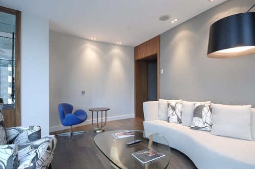 A modern living room with a curved white sofa, a blue armchair, a glass coffee table, and a black ceiling lamp.
