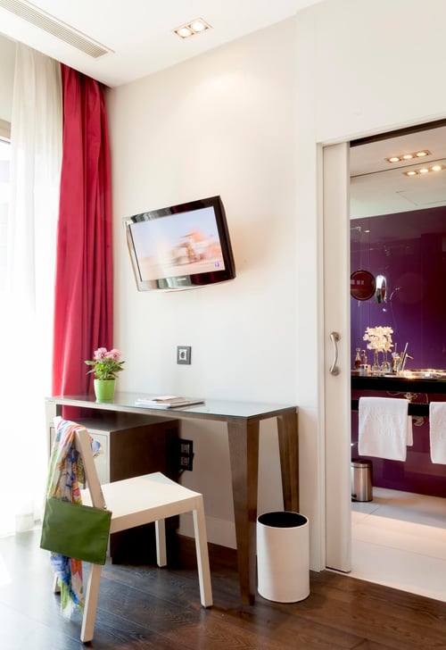 A modern room with a desk, a white chair, a TV mounted on the wall, red curtains, and access to a bathroom with purple walls