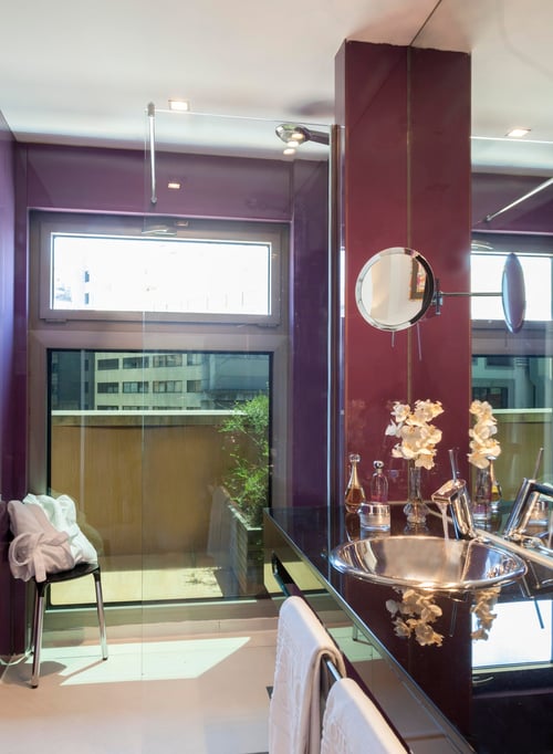 A modern bathroom with purple-toned walls, adjustable mirrors, and a metal sink with floral decorative accents. It includes