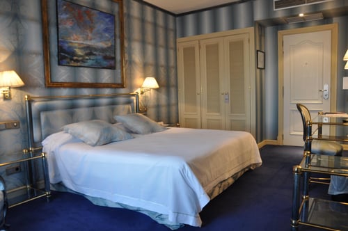 Room 414 features a double bed, blue-toned walls with a floral pattern, and a landscape painting. It includes wall sconces,