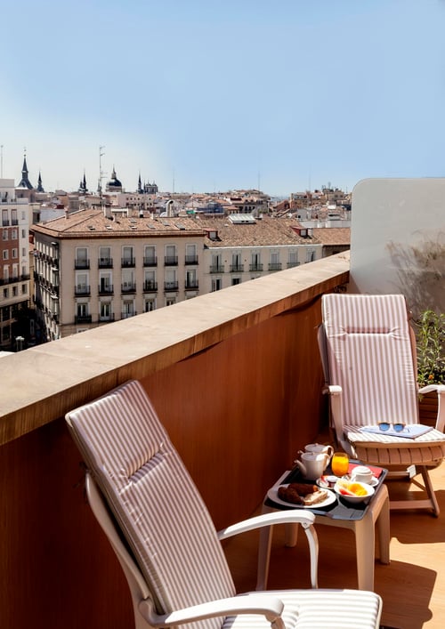 A terrace overlooking Madrid's historic buildings, with reclining chairs and breakfast served at a table. The sky is clear,