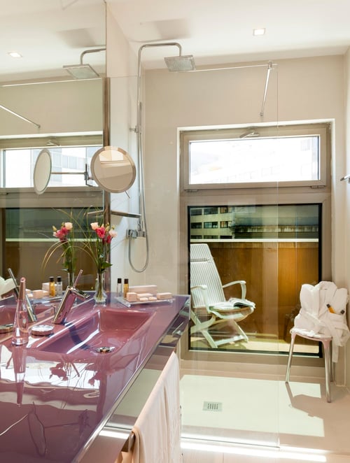 Modern bathroom with a burgundy-colored sink, a lighted mirror, a glass shower, and views of city buildings. Includes