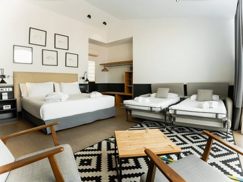 Habitación moderna con cama doble, sofá cama, mesas auxilares y decoración minimalista en tonos neutros y patrones