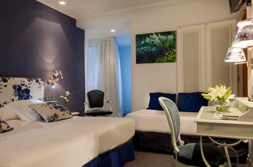 A triple room with two single beds and one double bed, decorated in shades of blue and white, with details such as lamps,