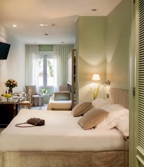 Triple room with a king-size bed and a sofa bed, decorated in neutral tones, with windows featuring white curtains and light