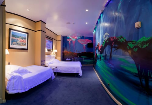 A triple room with two single beds, walls decorated with murals of underwater landscapes in shades of blue and green, and