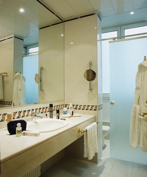 Modern bathroom with a countertop sink, large mirror, white towels, and accents in beige and gold tones. Includes toiletries