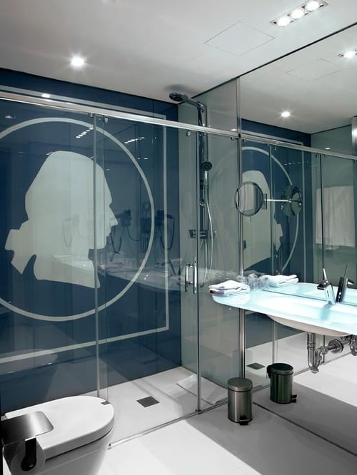 Modern bathroom with a glass shower enclosure, dark blue walls, and white bathroom fixtures. Includes a sink with a mirror,
