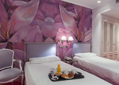 A room with two single beds, walls decorated with a mural of purple flowers, and a breakfast tray on the main bed. It