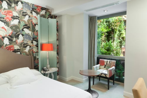 A room with a double bed, a wall decorated with a mural of geishas, and modern furniture, including a round table and a