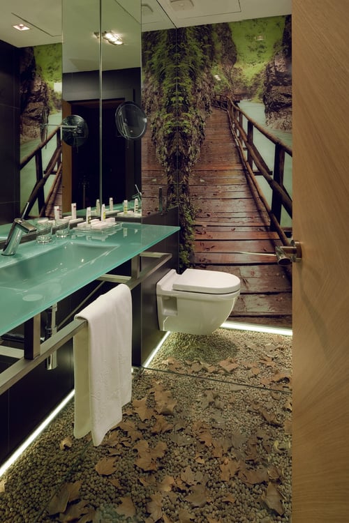 A modern bathroom with a wall decorated with an image of a wooden bridge in a natural setting, a floor featuring stones and