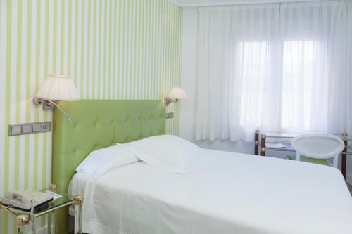 A bedroom with a white bed, a green headboard, and walls with light-colored vertical stripes. It features wall sconces,