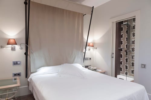 A bedroom with a white bed, wall sconces, and a beige curtain that separates the sleeping area. It includes a mirror with a