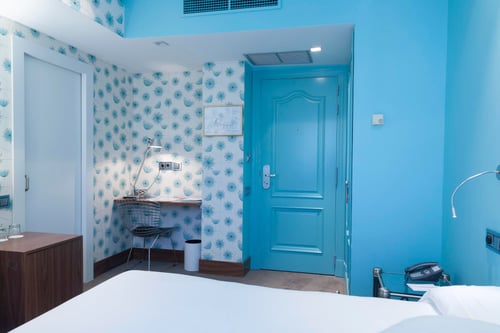 A room with blue walls, a door of the same color, and a work area featuring blue-and-white floral wallpaper, a lamp, and a