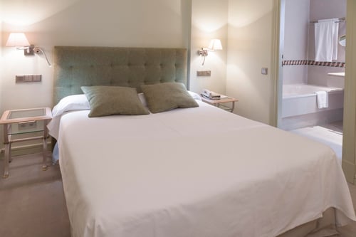 A bedroom with a double bed, a light green upholstered headboard, matching pillows, nightstands with lamps, and an open