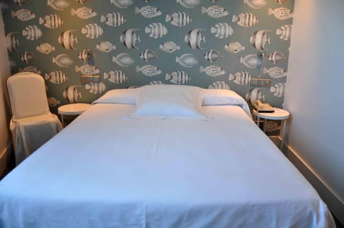 Room with a double bed and a wall decorated with fish-patterned wallpaper in shades of gray and blue. It includes