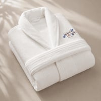 Luxury white bathrobe with embroidered Hotel Carmen logo, carefully folded on a bed with silk sheets. This